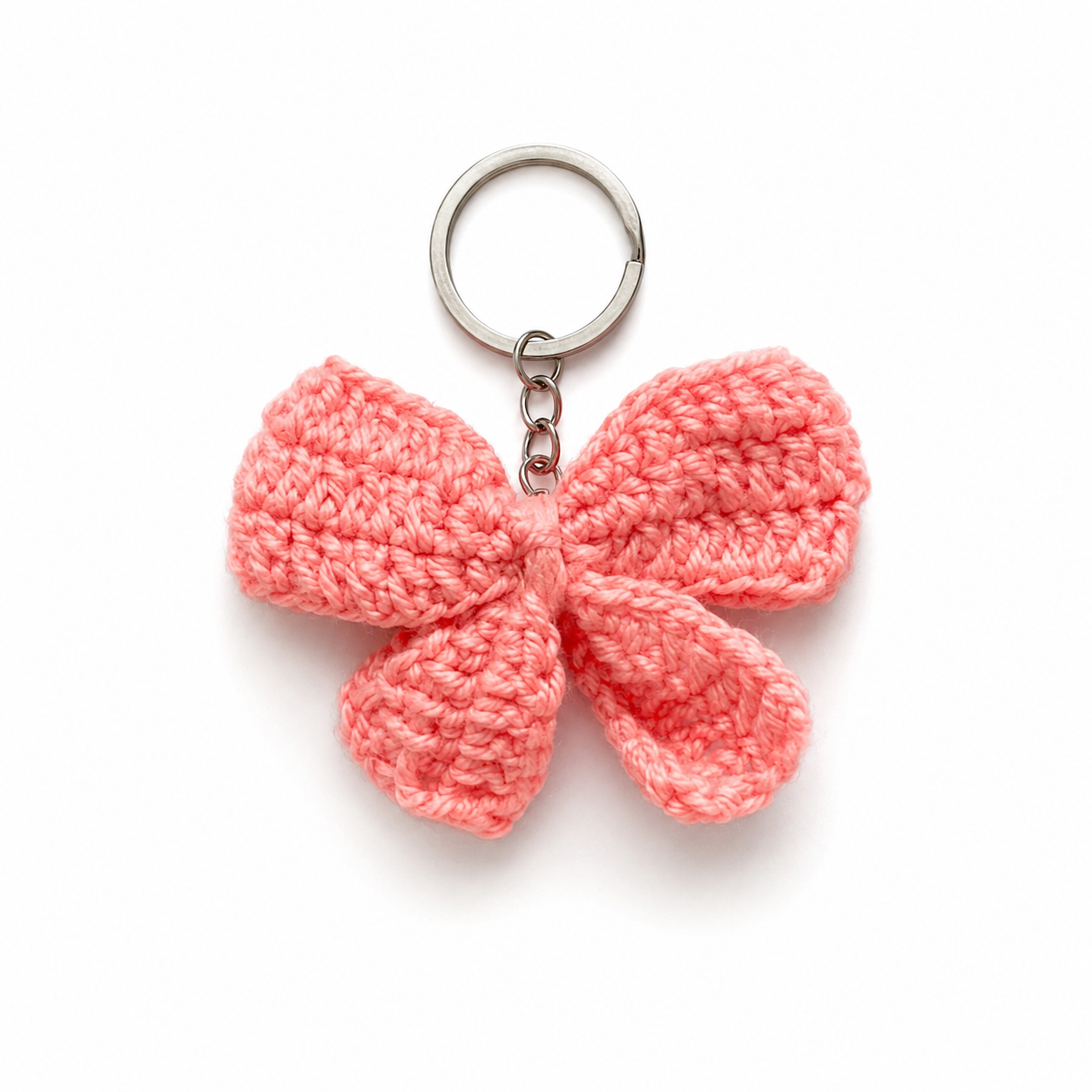 A crocheted bow keychain in a soft coral pink color, attached to a silver metal split ring and short chain, shown on a clean white background.