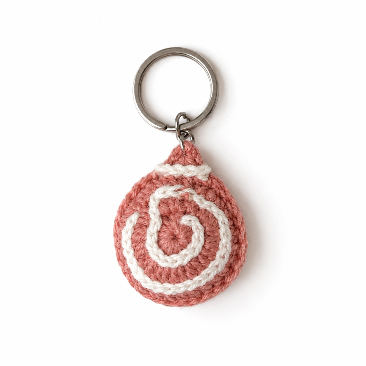 A crocheted keychain featuring a spiral pattern in dusty pink and cream yarn, attached to a silver metal split key ring, shown on a plain white background.