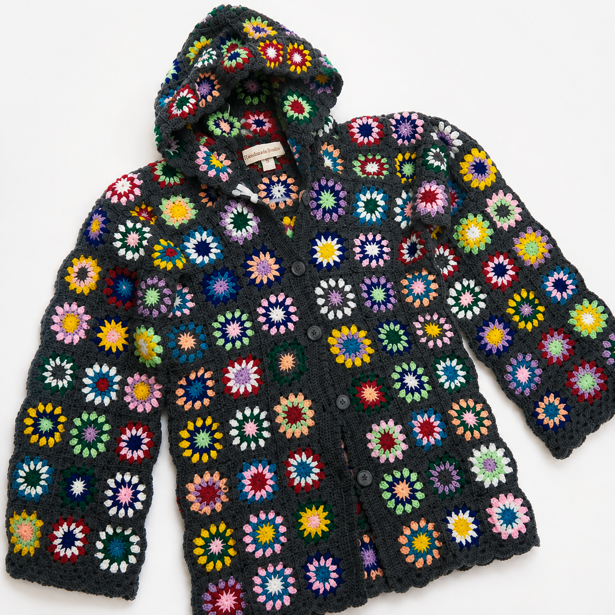 A handmade crocheted hooded cardigan featuring a black base covered in colorful granny square motifs, laid flat on a white background.